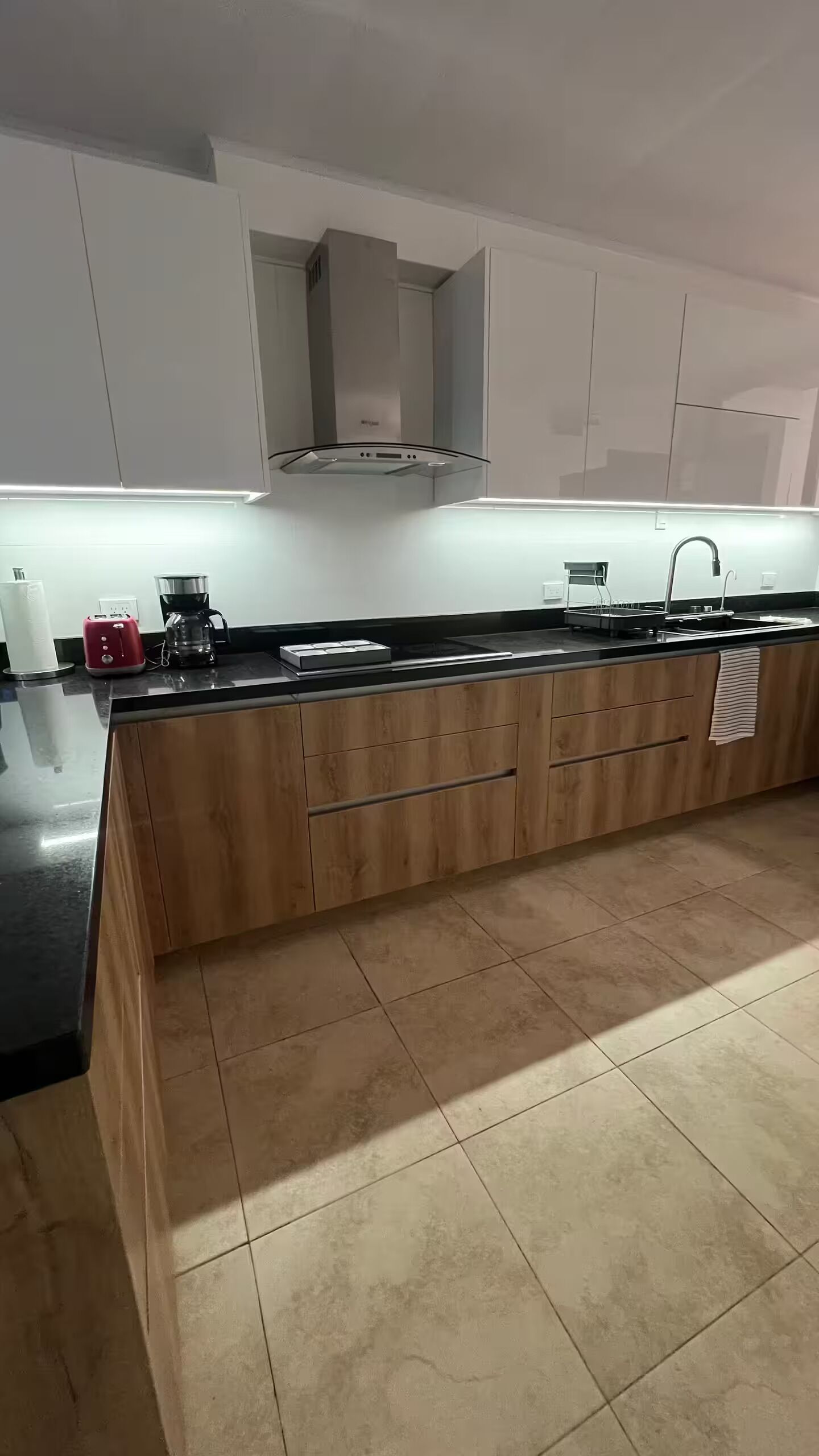 Una cocina moderna con armarios de madera, encimera negra y campana extractora de acero inoxidable.