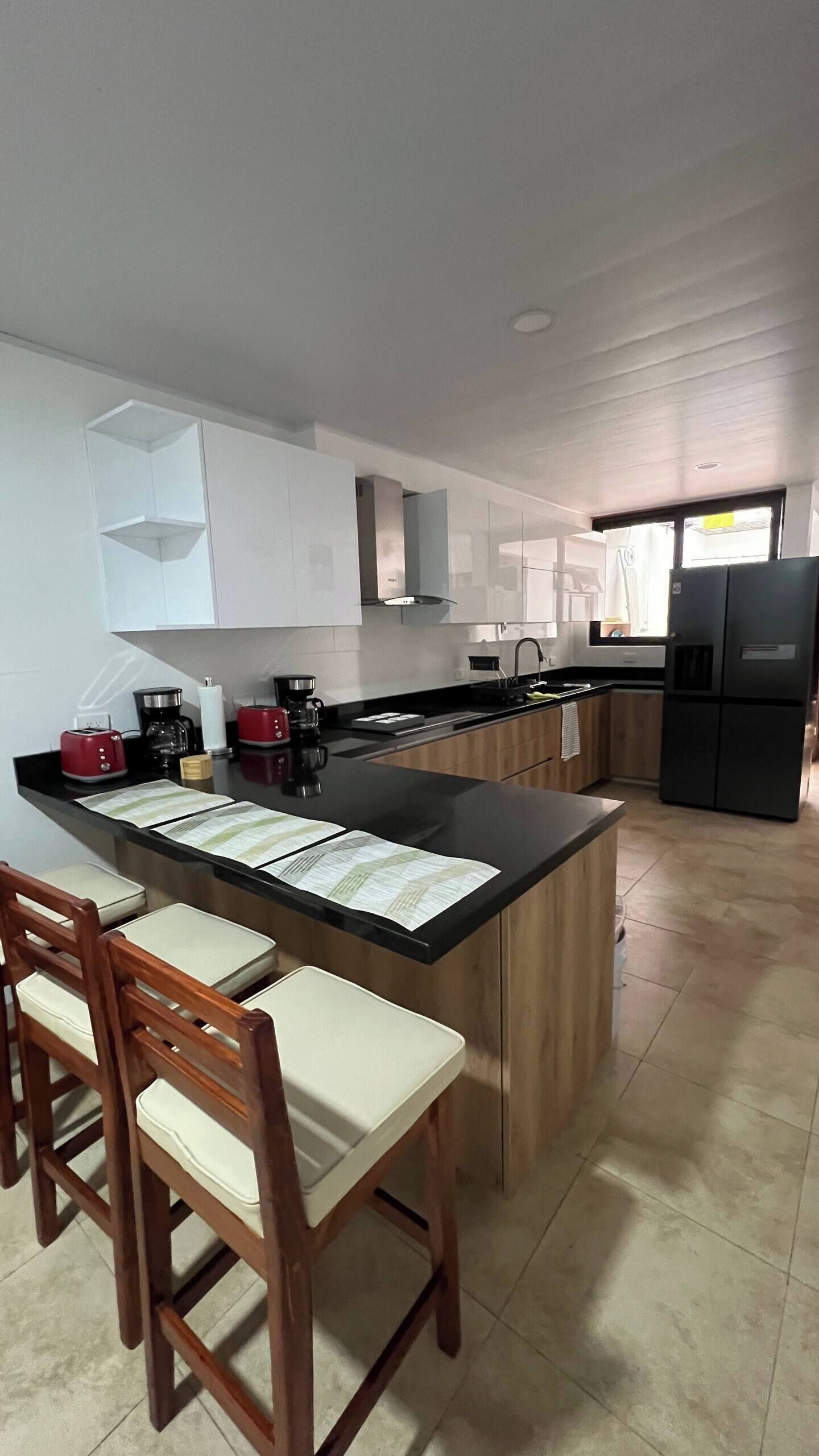 A modern kitchen with a central island, bar stools, and a refrigerator.