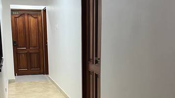 A hallway with a tiled floor, a wooden door with a number, and a ceiling with a recessed light fixture.