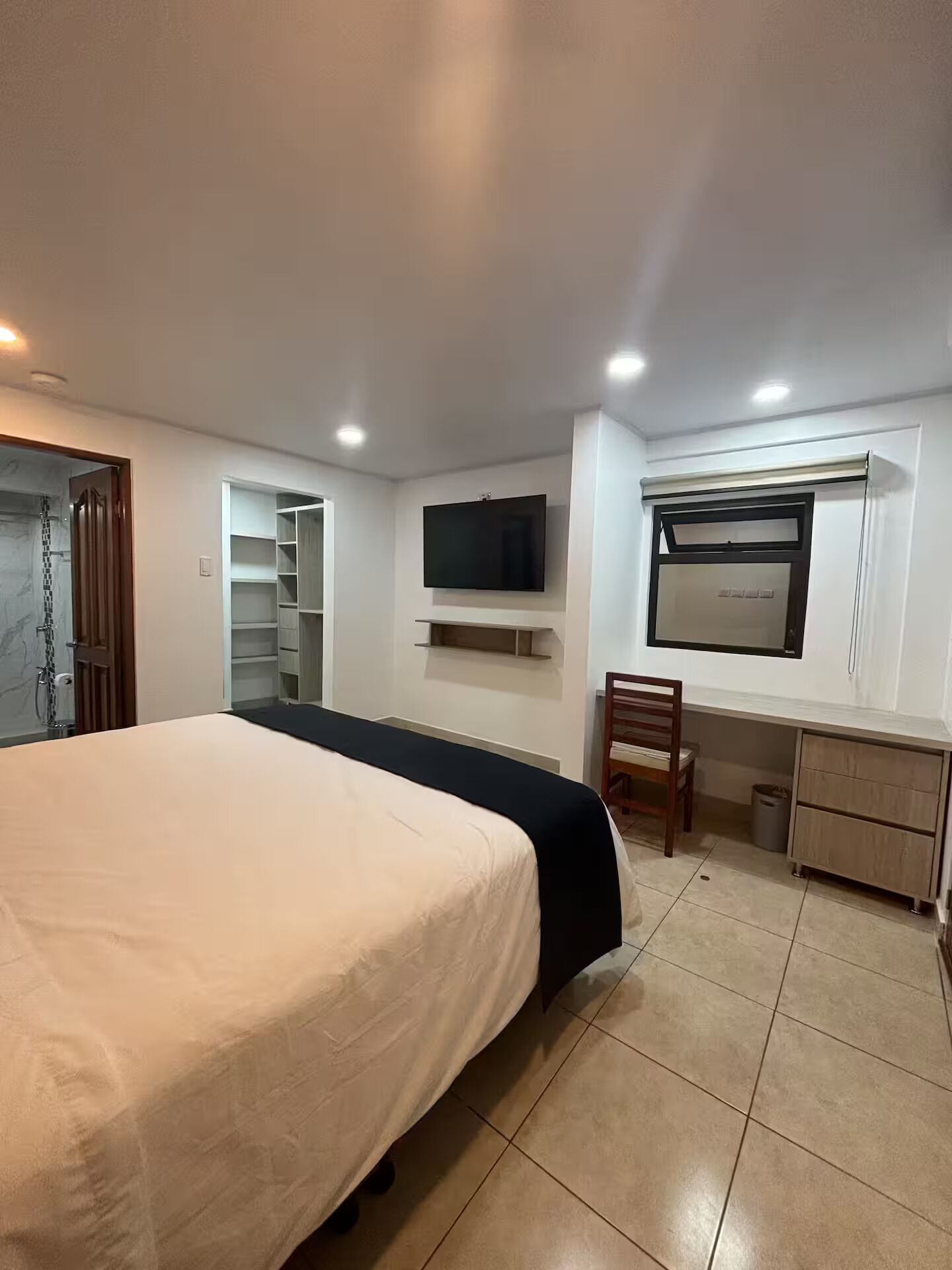 A bedroom with a bed, a TV, a desk, and a chair.