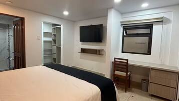 A bedroom with a bed, a TV, a desk, and a chair.