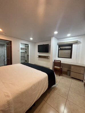 Ein Schlafzimmer mit Bett, Fernseher, Schreibtisch und Stuhl.