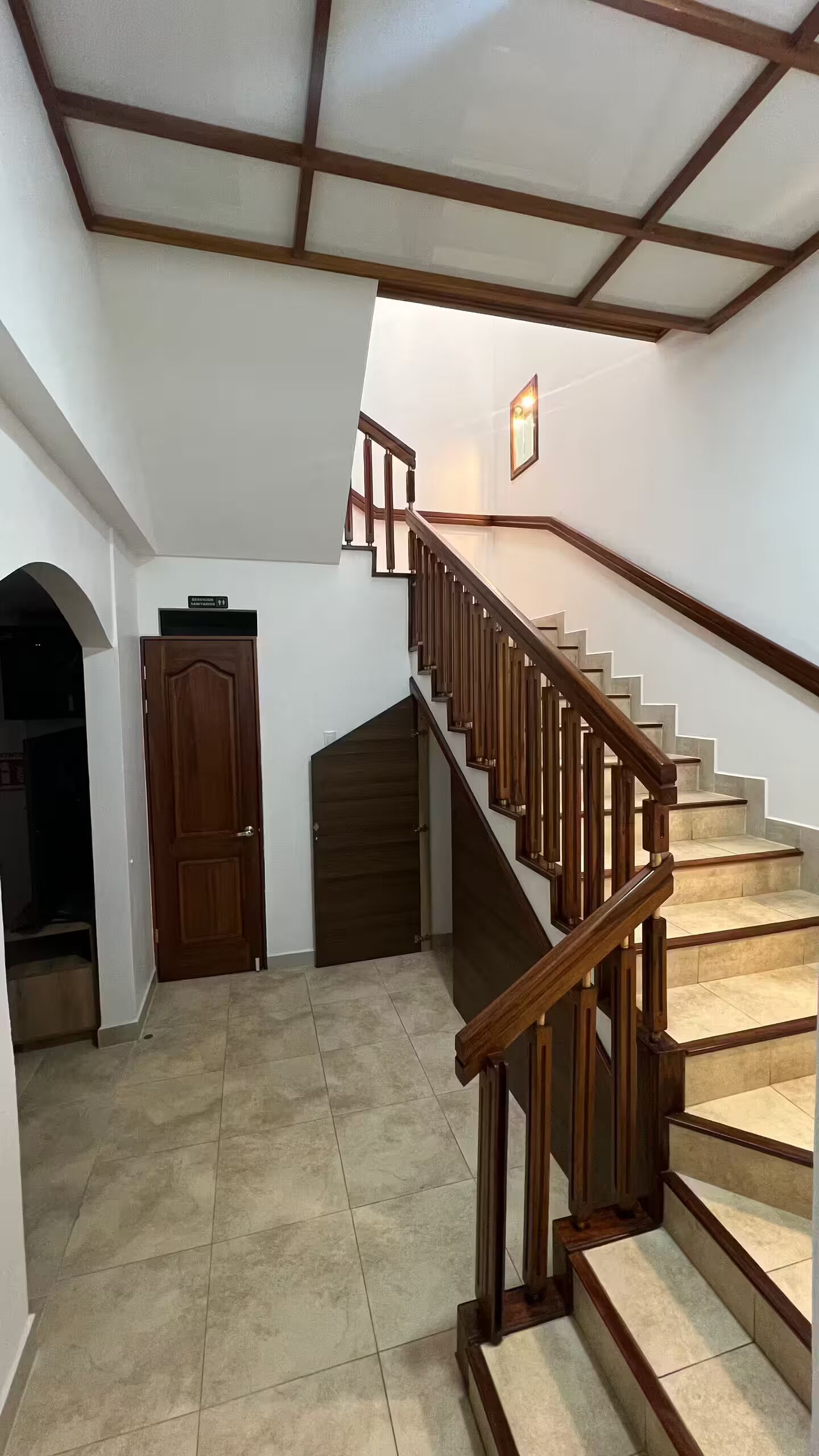 Una escalera de madera con barandillas y piso de baldosas que conduce a un nivel superior.