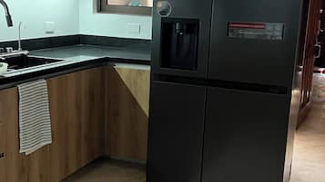 A kitchen with a black refrigerator, a sink, and wooden cabinets.
