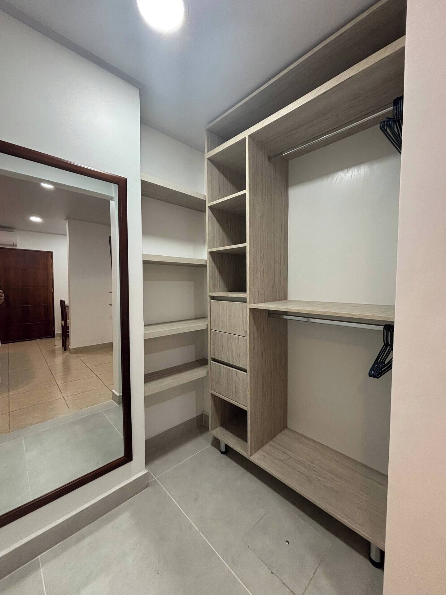 A walk-in closet with multiple shelves and drawers, a mirror, and a door leading to another room.