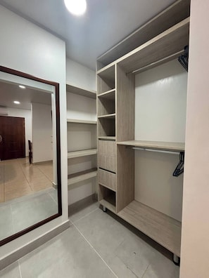 A walk-in closet with multiple shelves and drawers, a mirror, and a door leading to another room.