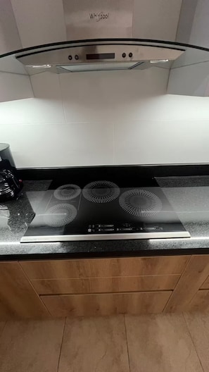 A kitchen with a black induction cooktop, a glass cooktop cover, and a Whirlpool hood.