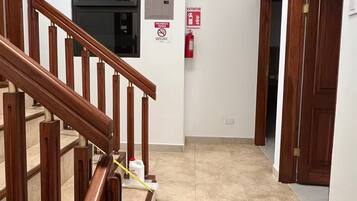 A hallway with a wooden staircase, a fire extinguisher, and a door on the right.