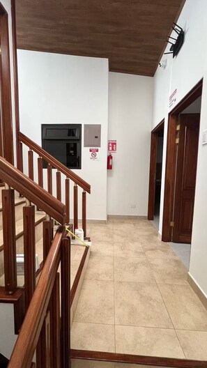 Eine Treppe mit Holzhandläufen führt zu einer Zwischenebene mit einem Feuerlöscher und einem Rauchmelder.