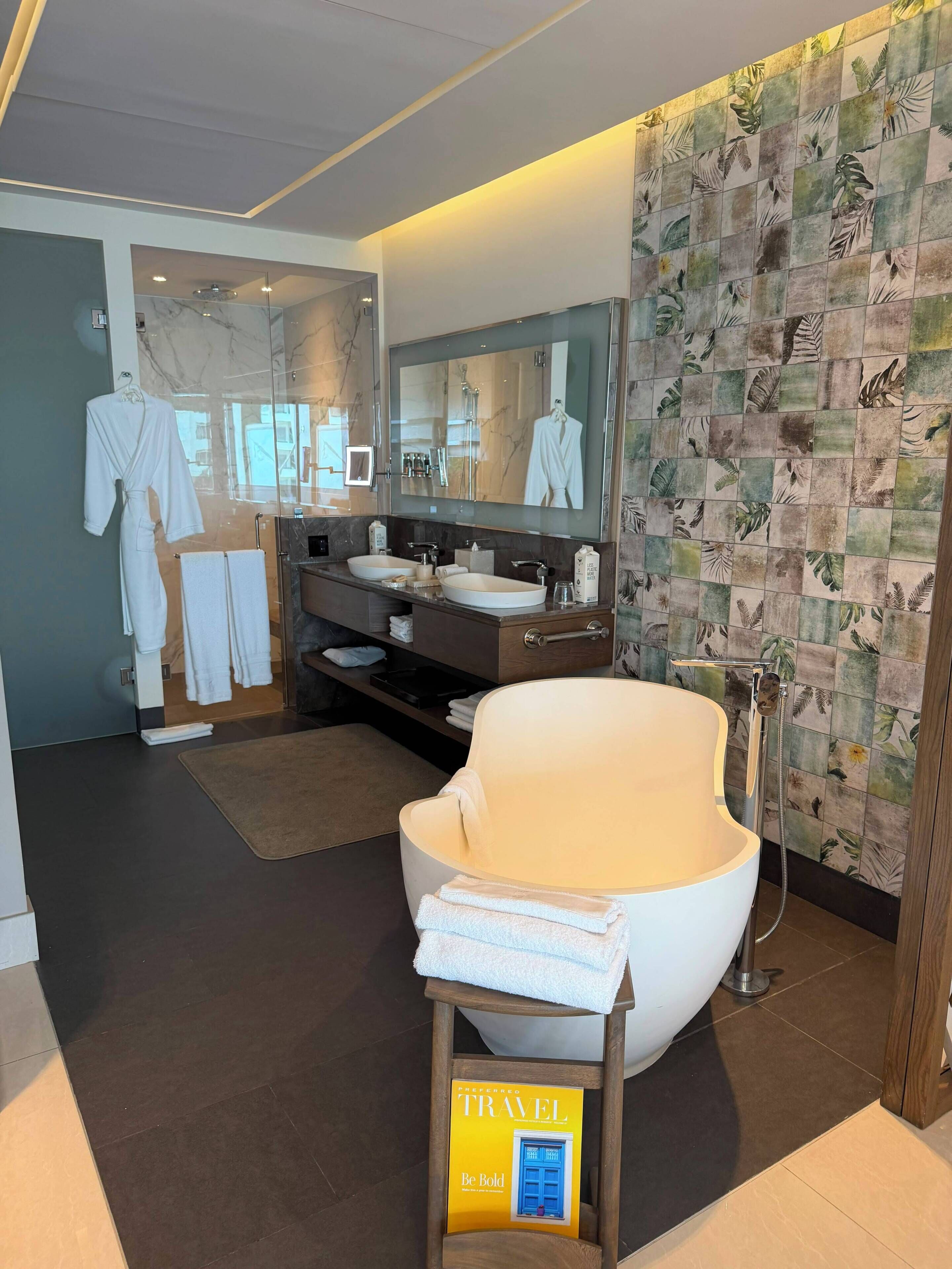 A modern bathroom with a large mirror, dual sinks, a shower, and a towel rack.