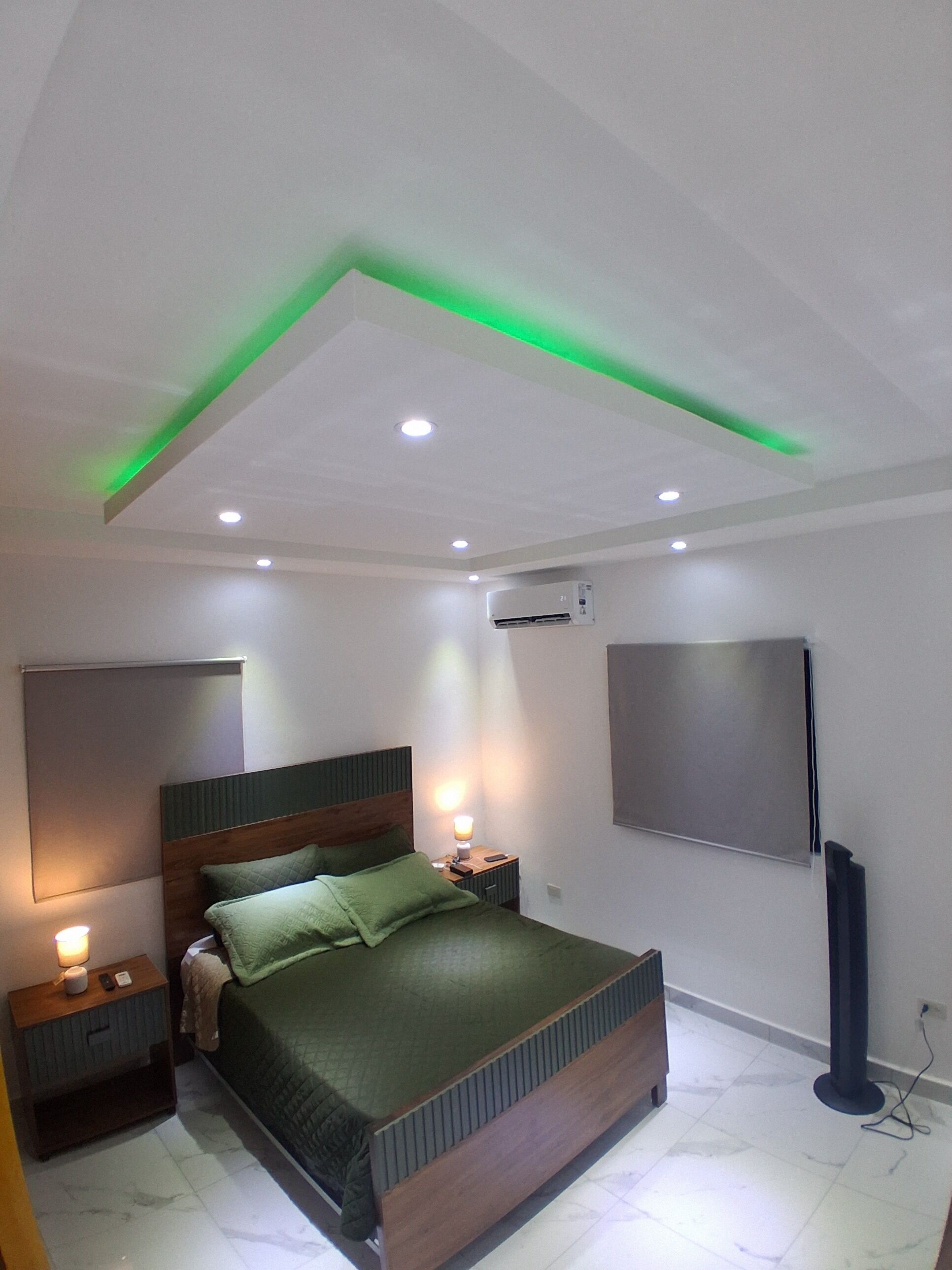 Un dormitorio moderno con cama, mesitas de noche, televisor y aire acondicionado.