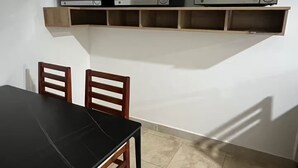 Un'area pranzo con un tavolo nero e sedie di legno, una parete bianca e uno scaffale con tre forni a microonde.
