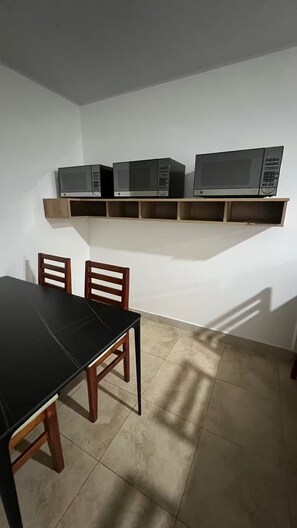 A dining area with a black table and wooden chairs, a white wall, and a shelf with three microwaves. - 102 El Mejor hospedaje en San José cerca al Estadio Nacional -Sabana Norte (San José)