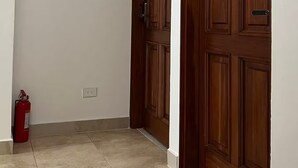 Un corridoio con due porte in legno, un estintore e un interruttore a muro.