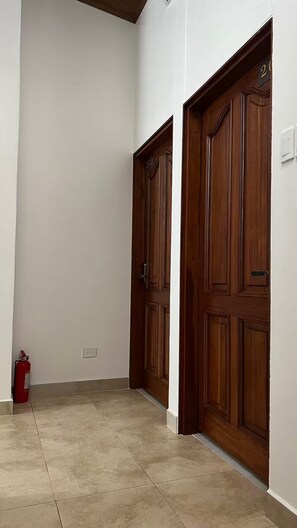 A hallway with two wooden doors, a fire extinguisher, and a light switch on the wall. - 102 El Mejor hospedaje en San José cerca al Estadio Nacional -Sabana Norte (San José)