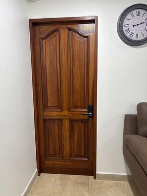 A wooden door with a number '102' above it, a wall clock, and a brown sofa.