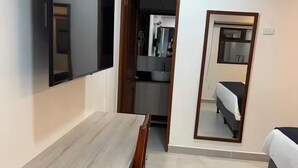 Una stanza con una scrivania in legno, un letto, uno specchio e angolo cottura.