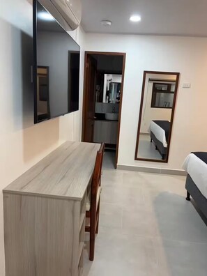 A room with a wooden desk, a bed, a mirror, and a kitchenette. - 102 El Mejor hospedaje en San José cerca al Estadio Nacional -Sabana Norte (San José)