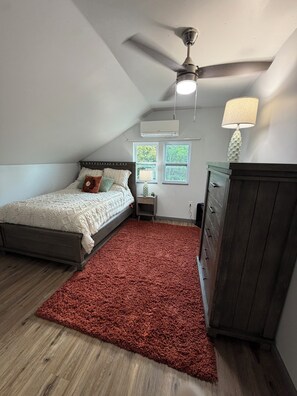 Ein Schlafzimmer mit einem Bett, einem Schminktisch, einem Nachttisch, einer Lampe und einem Deckenventilator.