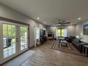 A spacious living room with a fireplace, a ceiling fan, and a large TV. - 7 Acre Hidden Hills Cabin 35 minutes from Nashville (Portland)
