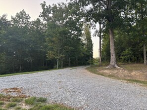 Ein Kiesweg führt durch ein bewaldetes Gebiet mit Bäumen und einer Holzkonstruktion.