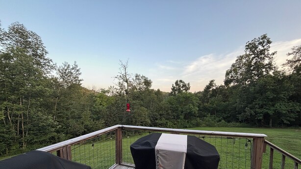 A wooden deck with a metal railing, a grill cover, and a table with a grill cover. - 7 Acre Hidden Hills Cabin 35 minutes from Nashville (Portland)
