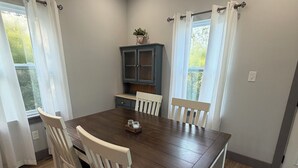 A dining area with a wooden table, white chairs, a cabinet, and a window with curtains. - 7 Acre Hidden Hills Cabin 35 minutes from Nashville (Portland)