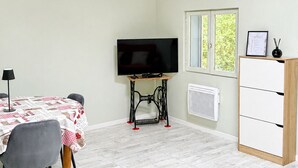 A room with a television, a sewing machine, a table with chairs, a window, and a cabinet.