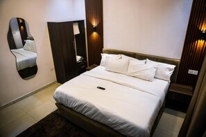 Een hotelkamer met een bed, spiegel, kledingkast en nachtkastje.