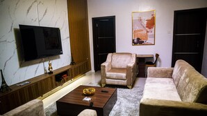 Uma sala de estar com televisão de tela plana, dois sofás, uma mesa de centro e um quadro na parede.