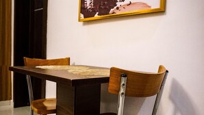 Uma área de refeições com uma mesa retangular e quatro cadeiras, uma delas com estrutura metálica.