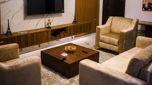 Uma sala de estar moderna com uma televisão de tela plana fixada em uma parede de mármore, um armário de madeira, um sofá, uma mesa de centro e um tapete felpudo.