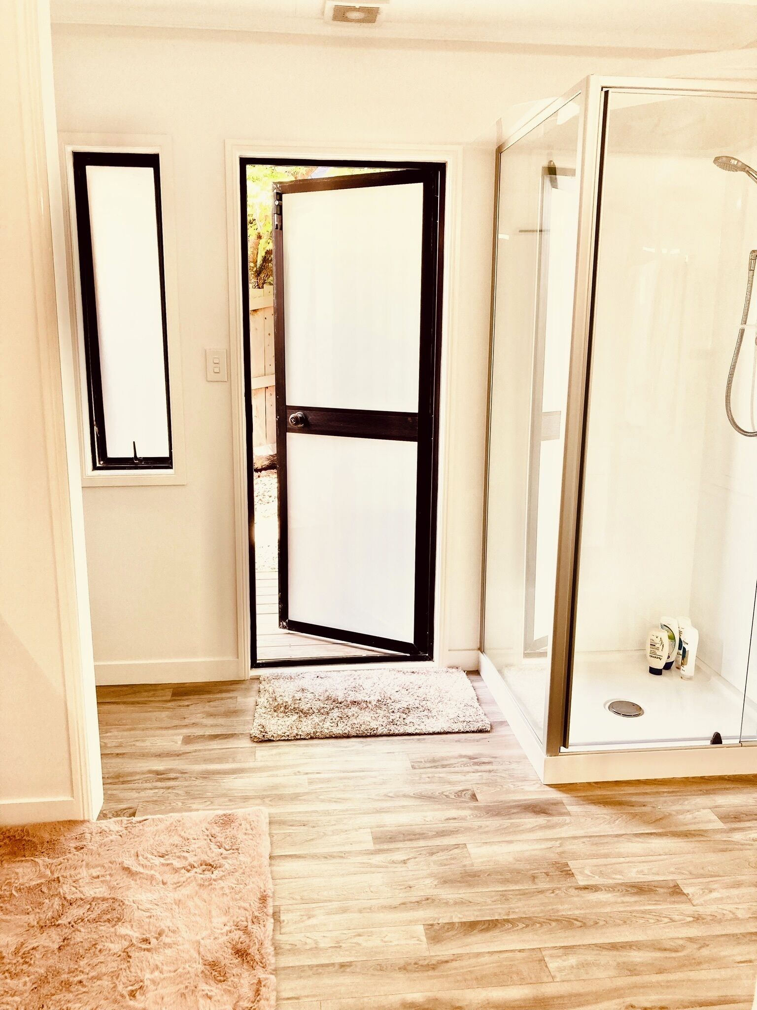 A room with a wooden floor, a white door, a glass shower enclosure, and a fluffy rug.