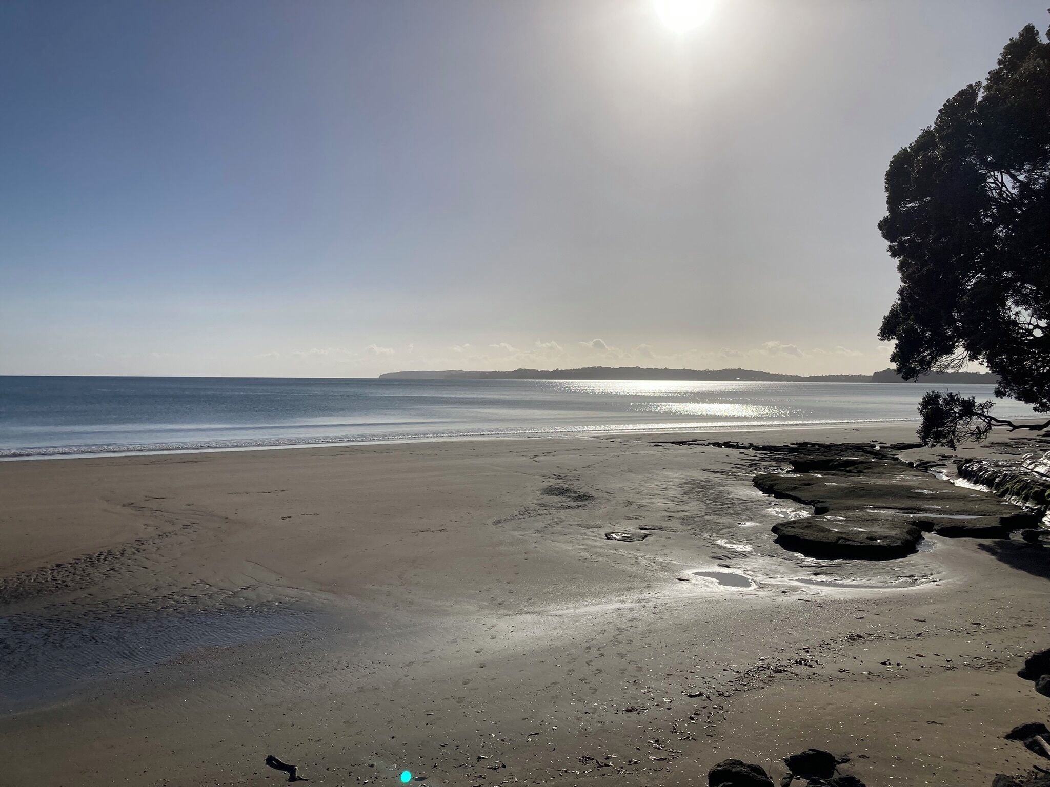 Une plage avec un ciel dégagé, une mer calme et une côte rocheuse.