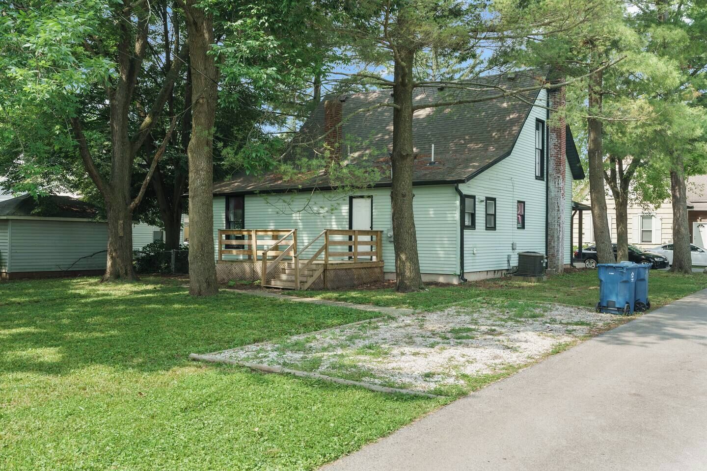 Une maison de plain-pied avec un porche à l’avant, une clôture en bois et une benne à ordures bleue.