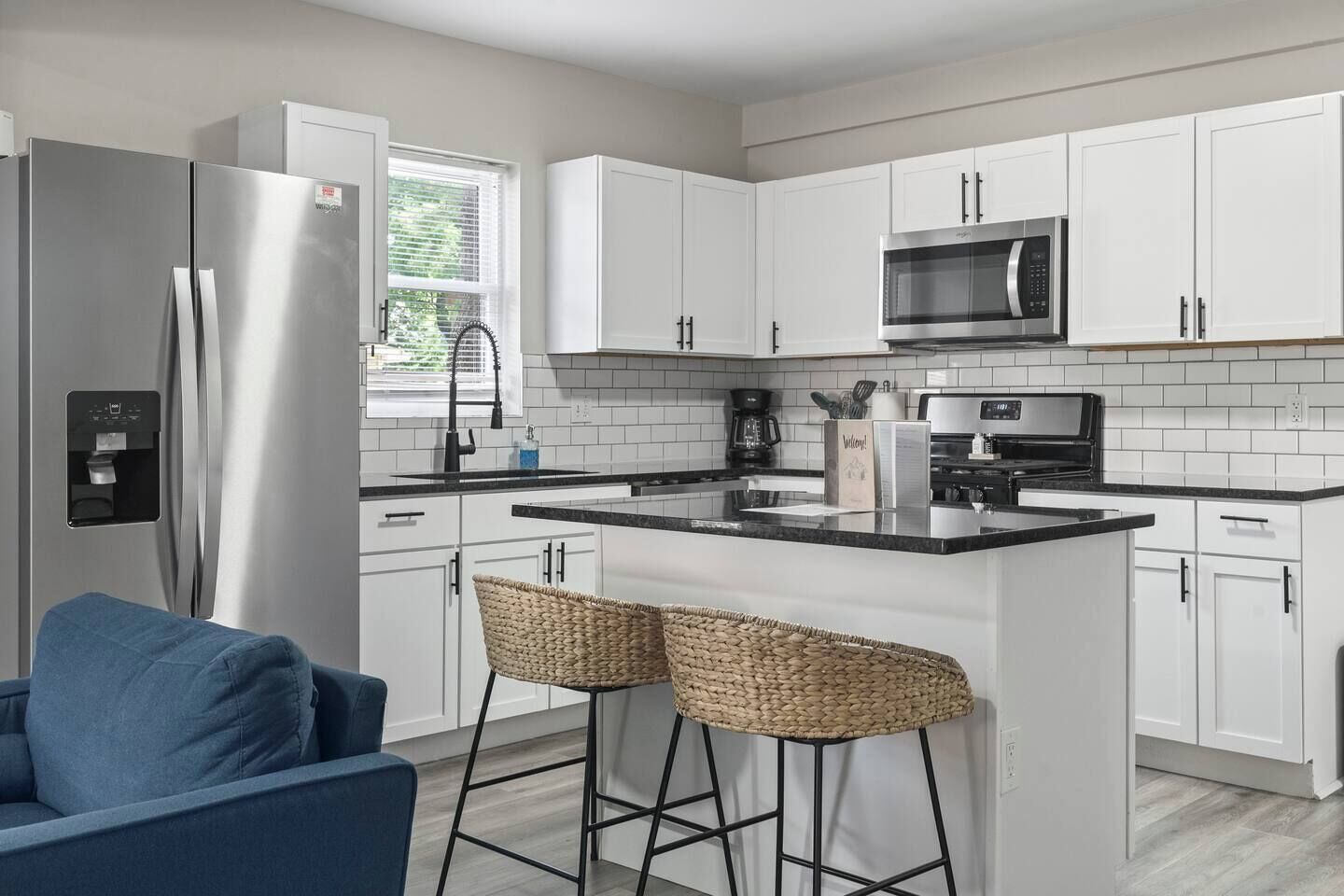 Une cuisine moderne avec des meubles blancs, des appareils en acier inoxydable, un comptoir noir et un tabouret de bar.