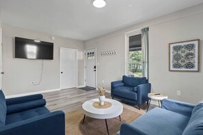 A modern living room with a flat-screen TV, blue sofas, a coffee table, and a large window with a view.