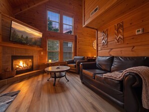 A cozy cabin interior with a fireplace, leather sofa, and a television mounted on the wall. - Sleeps 4, Romantic Chalet, Private Hot Tub, Jacuzzi Tub, Gas Fireplace (Gatlinburg)