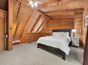 Une chambre à coucher avec un plafond en pente, un lit, une table de chevet, une lampe et un extincteur.