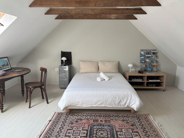 A bedroom with a bed, a desk, a chair, a nightstand, and a wall with a calendar.
