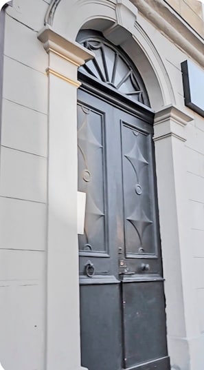 Eine Doppeltür mit dekorativem Design, eingebettet in ein Gebäude mit heller Fassade und einem Bogenfenster darüber.