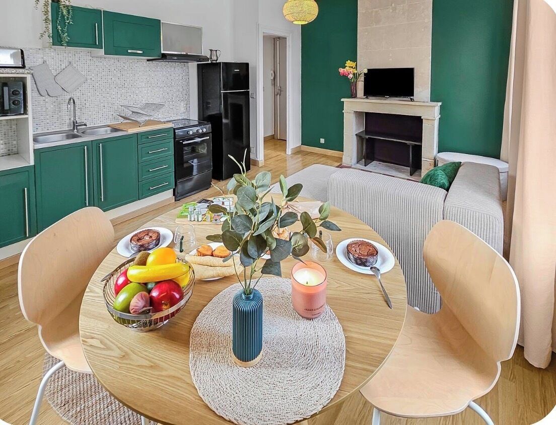 Uma cozinha moderna com armários verdes, uma mesa de jantar com cadeiras e uma sala de estar com lareira.