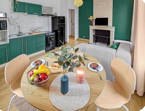 Uma cozinha moderna com armários verdes, uma mesa de jantar com cadeiras e uma sala de estar com lareira.