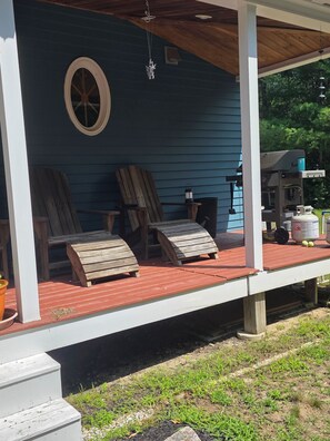Een overdekte veranda met twee houten Adirondack stoelen, een lantaarn en een barbecue.