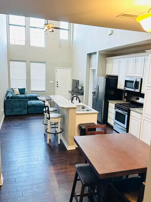 A spacious kitchen with a central island, a dining area with a table and chairs, and a living area with a sofa and chairs. - Modern home: easy airport access & near amenities (Odessa)