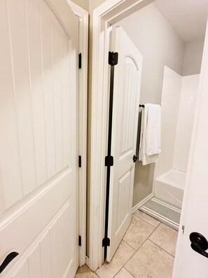 A hallway with white doors, a tiled floor, and a white towel hanging on a rack. - Modern home: easy airport access & near amenities (Odessa)