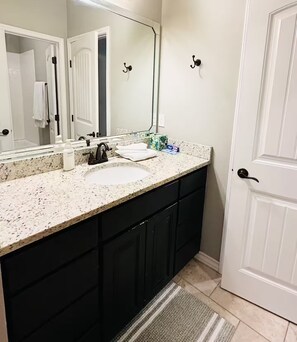 A bathroom with a white sink, dark cabinets, a large mirror, and a door with a handle. - Modern home: easy airport access & near amenities (Odessa)