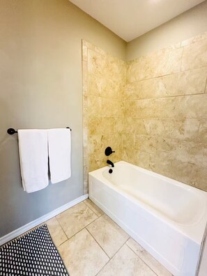 Ein Badezimmer mit einer Badewanne, zwei Handtüchern und einer Fußmatte mit Struktur.