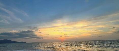 A beach with the ocean and a distant landmass under a sunset sky.