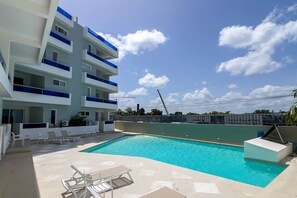 A modern building with a swimming pool, outdoor seating, and a clear sky. - ANYA 2 Two BDR Family and friend Apartment with pool (San Rafael del Yuma)